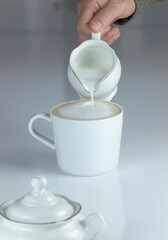 Adult man pouring milk into coffee on white table