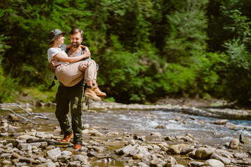White man holding happy young woman in his hands by river in nature