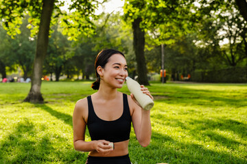 Young asian woman drinking water from bottle during workout in park
