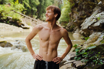 Young ginger man smiling while resting by mountain river