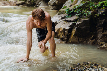 Young man picking up stones by the mountain river