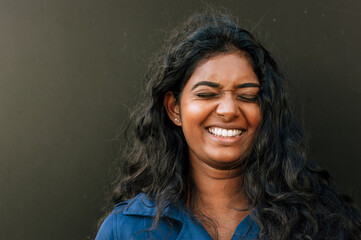Obraz premium Cheery indian woman laughing with eyes closed while standing over dark background