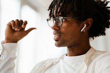 Young african man using earphones while sitting indoor