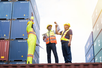 Group of male container yard workers standing on container box control loading containers boxes from cargo freight ship at commercial dock site. Delivery goods from cargo freight ship