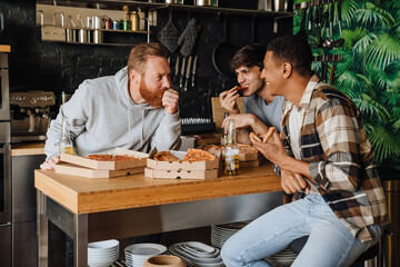 Cheerful male friends with pizza and beer talking while sitting at the table