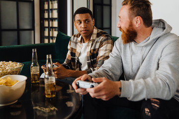 Two excited men playing video games and drinking beer in living room