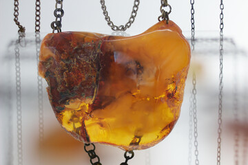 Beautiful piece of amber hangs on silver chains in a glass case on a white background