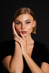 Young woman posing with folded hands on her cheek isolated over black background