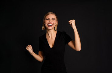 Cheerful woman with raised hands standing isolated over black background