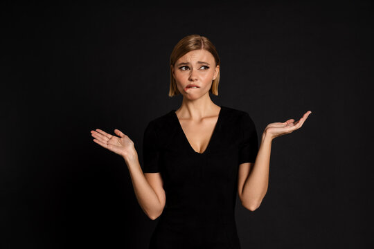 Confused Woman Holding Copyspace On Two Palms Bitting Her Lips Isolated Over Black Background