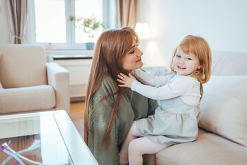 Attractive woman and little girl sitting on comfortable couch at home. Young mother talking communicates with small adorable daughter. Best friends happy motherhood weekend together with kid concept