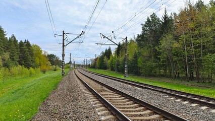The railway rails are laid on reinforced concrete sleepers and sprinkled with rubble. The railway is electrified and there are concrete poles with wires along the rails. Nearby there are grassy lawns