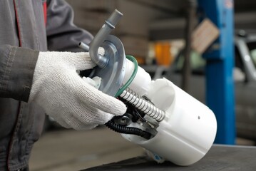 An auto mechanic holds a new fuel pump in his hands. Repair of the fuel and exhaust system of the...