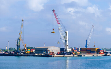 cargo sea port with cranes, container stacks and trucks with goods, sea hub terminal from seashore