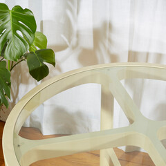 Vintage retro 1970s off-white dining table. Space age 1970s cream dinette table. Closeup view of a white glass top table in front of a white curtain surrounded by houseplants.