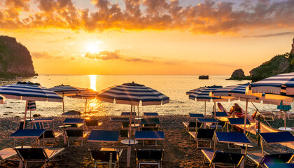 morning or evening landscape with nice beach with deck chairs and umbrellas during sunrise or sunset with amazing sea with rocks and beautiful clouds on background