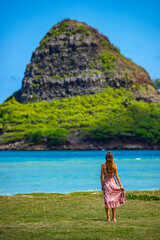 girl in long dress walks along seashore in kualoa regional park on oahu, hawaii, overlooking...