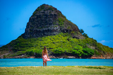 girl in long dress walks along seashore in kualoa regional park on oahu, hawaii, overlooking...