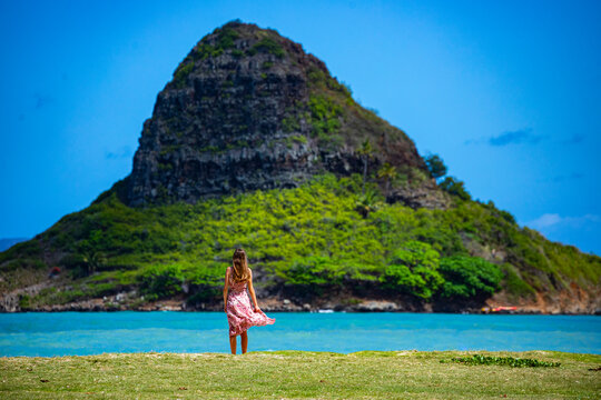 girl in long dress walks along seashore in kualoa regional park on oahu, hawaii, overlooking mokoli'i island with mighty mountain in background, holiday in hawaii islands