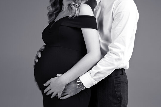 pregnant woman with her husband on a grey background in a studio, studio pregancy shoot, black and white photo