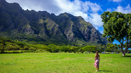 girl in long dress walks on grass at kualoa point on oahu, hawaii, overlooking mighty green mountains, romantic holiday in hawaii islands