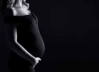 Beautifil silhouette of a pregnant woman with highlight on belly, woman in black, black and white photo, studio pregnancy shoot