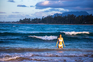 beautiful girl in a white bikini swims in the ocean on a paradise beach on oahu in the hawaii islands during sunset, holiday in hawaii, relax on the beach on oahu