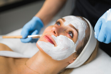 closeup side view of a charming blue-eyed Caucasian woman having a face cleaning procedure with a cosmetologist. High quality photo