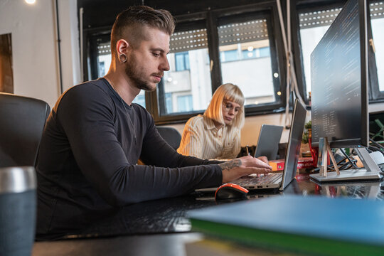 Casual male programmer sitting at the desk and trying to resolve the problem in code.