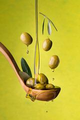 ladle with olives and oil on a green background. Olives, extra virgin olive oil and olive leaves float in the air