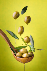 ladle with olives and oil on a green background. Olives, extra virgin olive oil and olive leaves float in the air