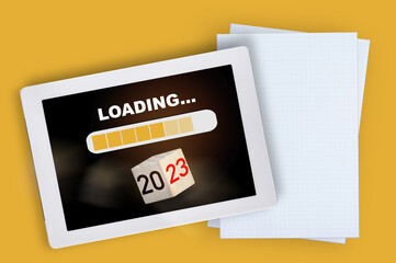 New year 2023 loading on computer digital tablet with white grid paper on yellow background