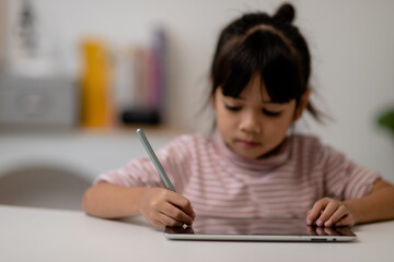 Asian little cute girl touching the digital tablet screen on the table