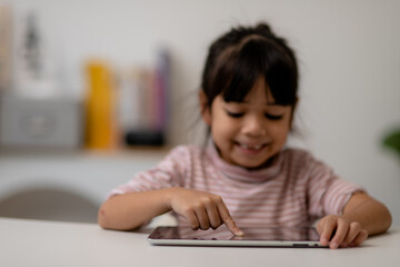 Asian little cute girl touching the digital tablet screen on the table