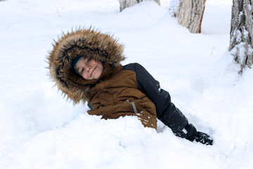 Active games in nature in winter. The boy is fooling around, buried in the snow. He looks at the...