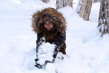 Active games in nature in winter. The boy plays in the snow mountain. He looks at the camera.