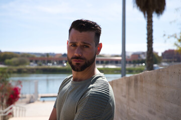 Handsome young man with blue eyes is standing on the stairs leading down to the river in the park. The man is on holiday in a European city. Travel and holiday concept.