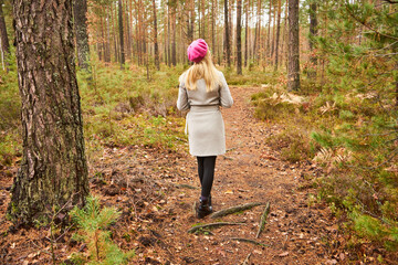 kobieta w różowym berecie i siwym płaszczu na spacerze w lesie  - obrazy, fototapety, plakaty
