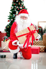 Happy smiling Santa Claus holding gift box under Christmas tree in white living room , Santa giving present to camera, celebrating happy Christmas winter holiday