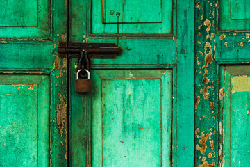 Close up of old green wooden door with latch and lock. It represents concept of antique, decadence, degeneration, secret, concealment, hidhing and ancient.