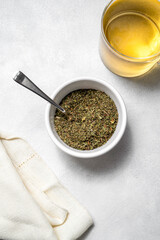 Green herbal tea mix, dried plants blend in bowl, on bright background