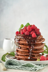 Chocolate Pancakes. Pancakes with fresh raspberry with chocolate glaze or toppings in gray bowl on light gray table background. Homemade classic american pancakes. Page for magazine concept.