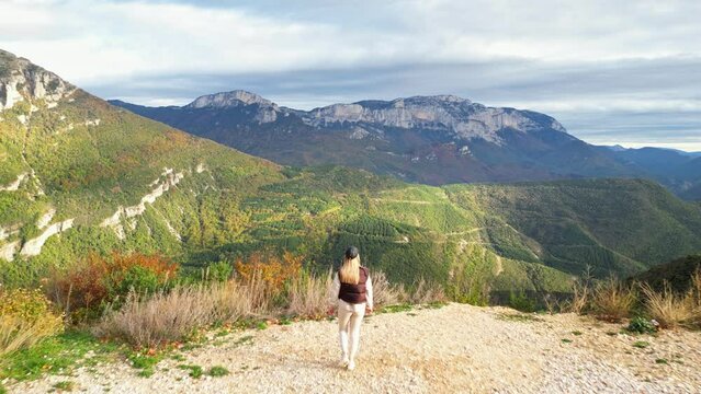 Young woman walking admiring the panoramic view from the Col de Rousset of the Vercors hills, the marly hills and the Val de Drome valley, France. Autumn View of the surrounding mountains and forests 