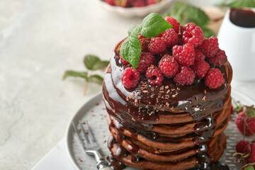 Chocolate Pancakes. Pancakes with fresh raspberry with chocolate glaze or toppings in gray bowl on light gray table background. Homemade classic american pancakes. Page for magazine concept.