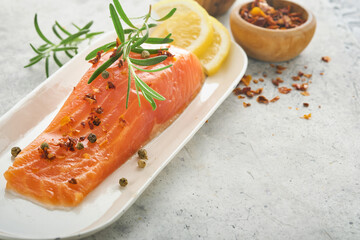 Salmon fish piece. Fresh raw salmon fish piece on marble board stand with herbs and lemon on light grey background. Seafood or menu concept. Top view.