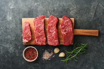 Raw steaks. Top blade steaks on wood burning board with spices, rosemary, vegetables and...