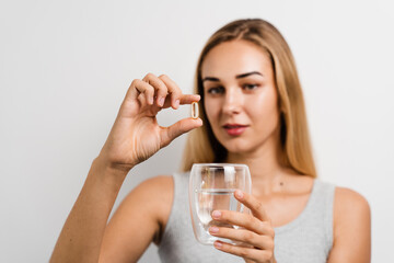 Girl with Omega-3 capsule and cup of water is taking a BADS capsule on white background. Biologically active dietary supplements. Taking vitamin D for building and maintaining healthy bones.