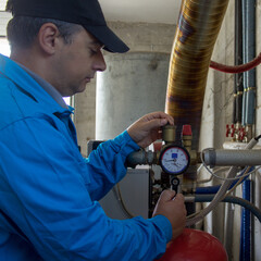 Plumber in working clothes repairing and maintaining a house boiler. Turning on the boiler in anticipation of winter
