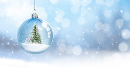 Fototapeta na wymiar Weihnachtskugel mit Weihnachtsbaum hängend vor unscharfem Schneehintergrund