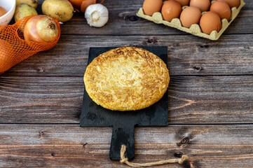 Top view, still life. Spanish potato omelette with some ingredients, on a wooden background. Space for text.
